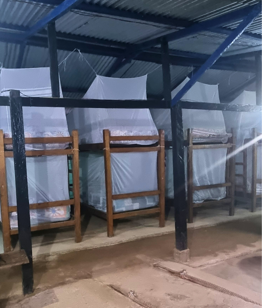 Rows of simple jungle bunk beds with mosquito nets in an open-air wooden shelter during the Lost City Trek.