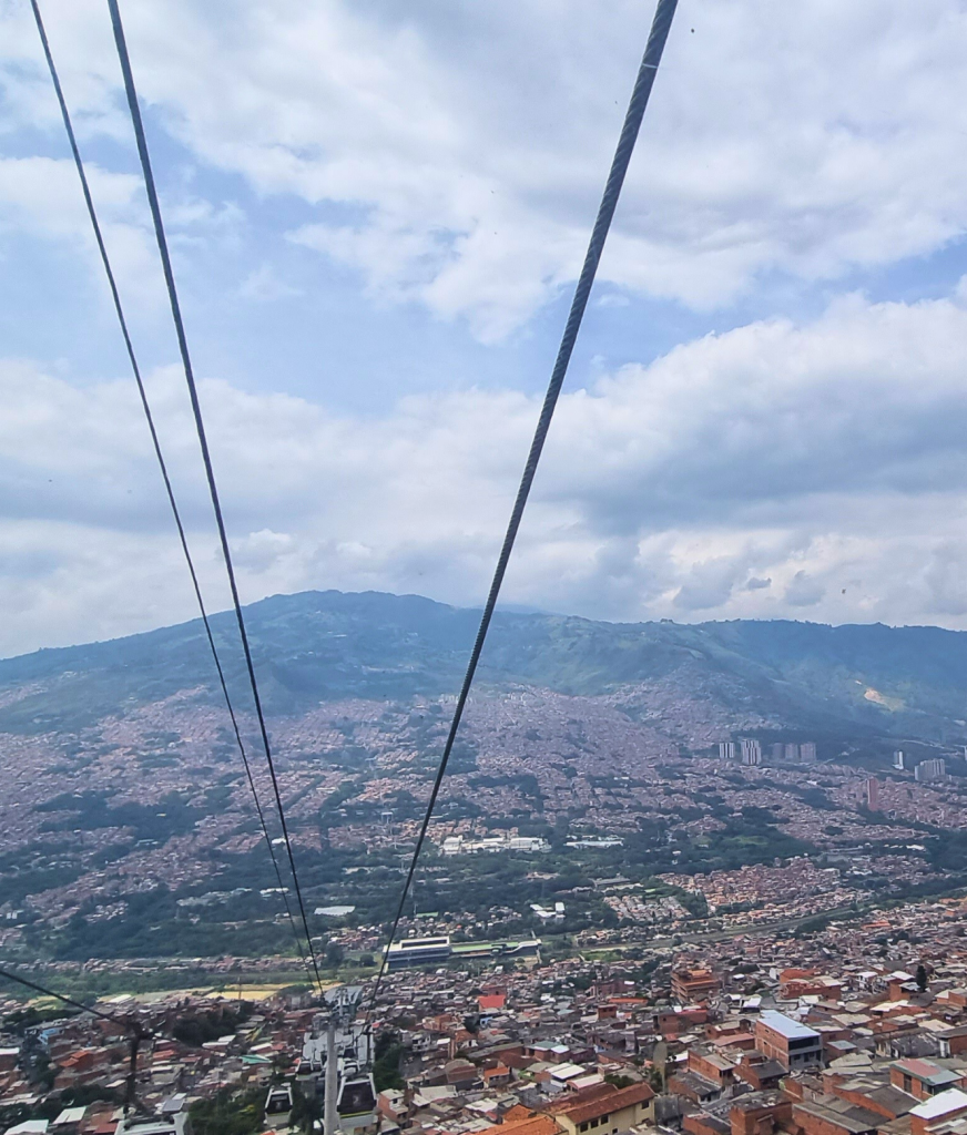 A stunning view of Medellín from the cable car, with the city nestled between lush green hills under a cloudy sky.