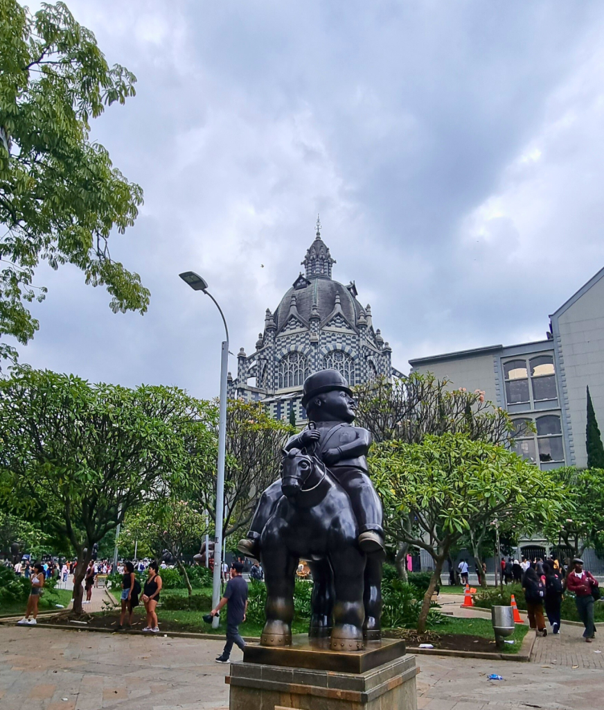 A sculpture by Fernando Botero in Bogotá's Botero Plaza, with the unique block-patterned Palace of Justice visible in the background.