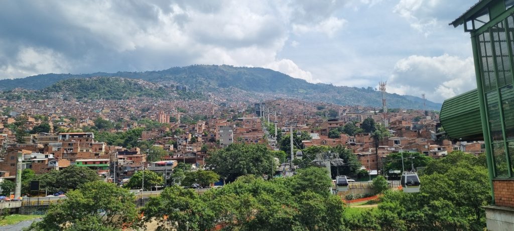 Panoramic view of Medellín from the cable car, showing the sprawling city nestled between lush green mountains under a cloudy sky.