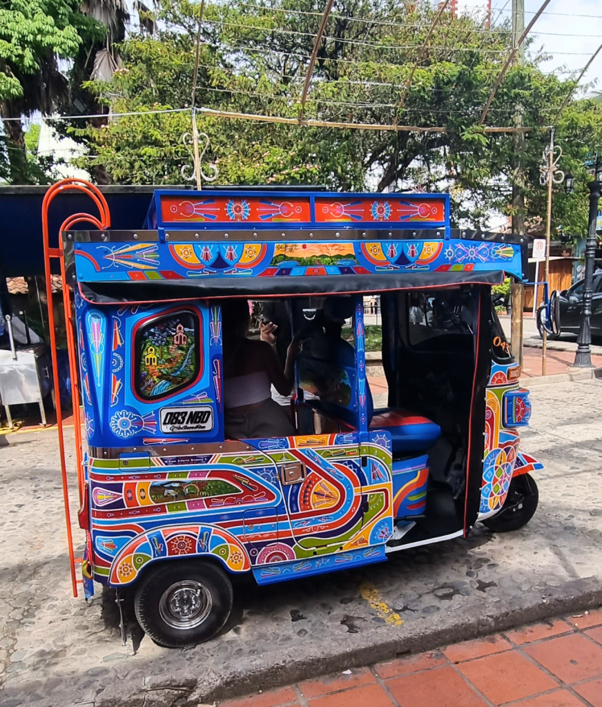 A vibrant, colorful tuktuk in the streets of Guatapé, adding to the town's lively atmosphere with its bright colors and unique charm.